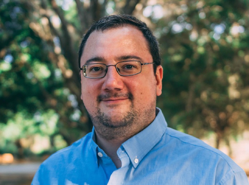 James Shank, outdoors, in a blue shirt and glasses. 2023.